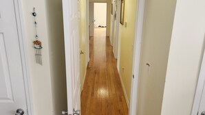 Un pasillo estrecho con suelo de madera, paredes blancas y una puerta a la izquierda.