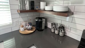 A kitchen with white tiled walls, wooden shelves, and a black countertop. - LAKE THERAPY- Cozy Lakeside with Beautiful Sunsets! (Temple)