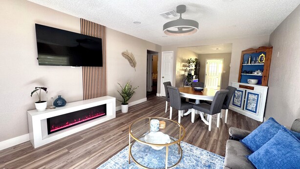 Ein modernes Wohnzimmer mit Flachbildfernseher, Kamin, Essbereich mit Stühlen und einer Couch mit blauen Kissen.
