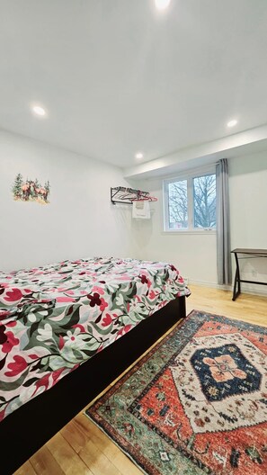 A bedroom with a bed, a rug, a window, and a wall-mounted drying rack. - Spacious Family Home | 15 Min Downtown, Near Dix30 (Brossard)
