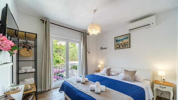 Ein Hotelzimmer mit einem großen Bett, einem Balkon mit Blick, einem Ablagefach mit Handtüchern und einem Gemälde an der Wand.