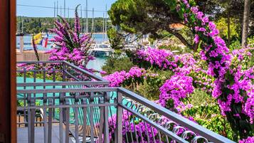 Un balcon doté d’une balustrade en métal, donnant sur une marina où sont amarrés des bateaux, avec un ciel bleu dégagé.