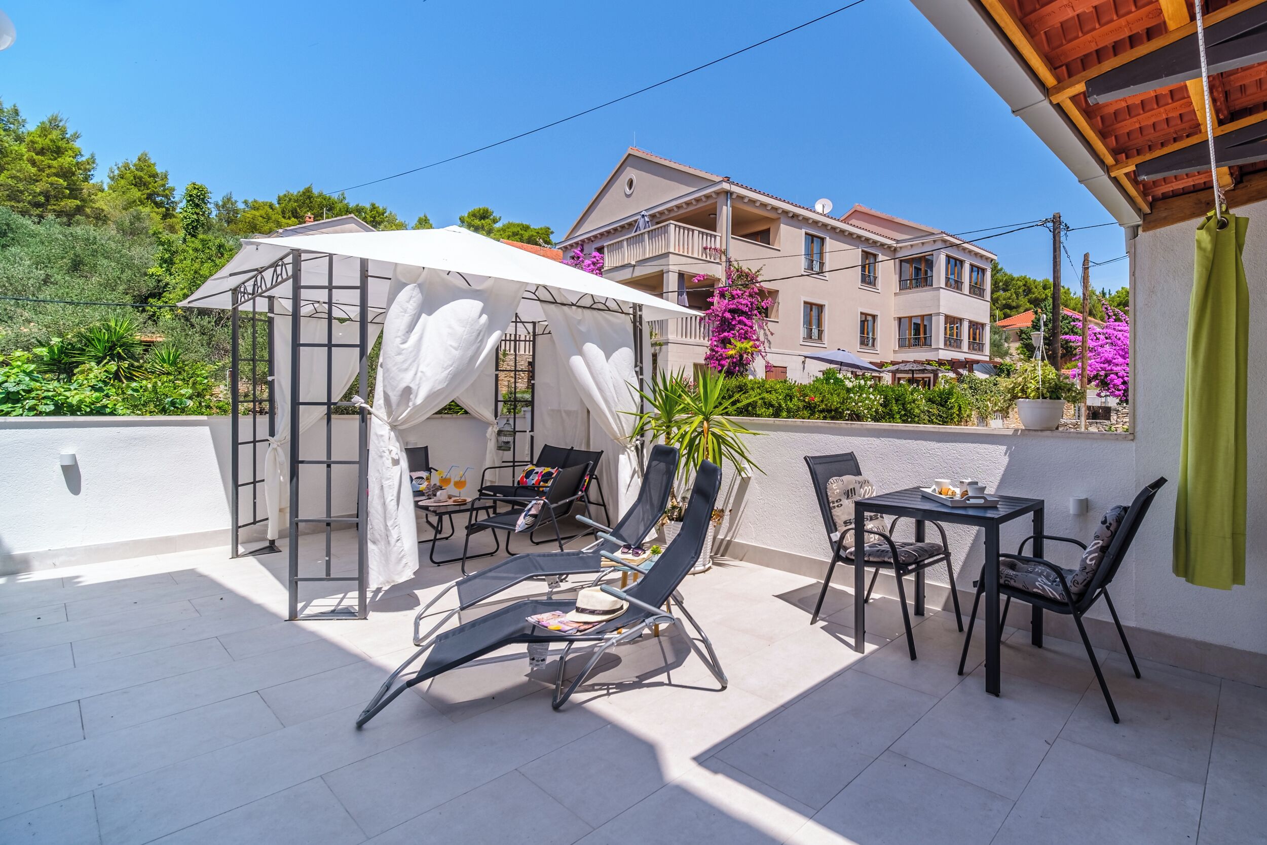 A terrace with a covered seating area, outdoor furniture, and a view of a multi-story building.