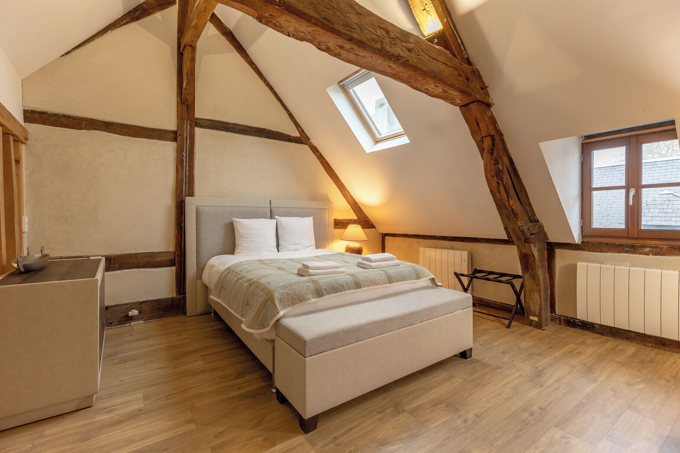 A bedroom with a sloped ceiling, a skylight, a bed with pillows, a bedside table, and a radiator.