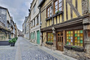 A narrow cobblestone street lined with historic buildings, some with visible shop fronts and windows. - Maison 1505 | Authentic 16th-century shipowner’s house in the city center (Honfleur)