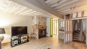A living room with a TV, fireplace, and wooden floors. - Maison 1505 | Authentic 16th-century shipowner’s house in the city center (Honfleur)