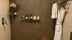 A small, tiled shower area with a toilet and a shelf with toiletries. - Hanuman Heritage (Chikkamagaluru)