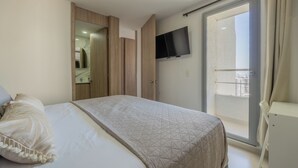 Quarto com cama, televisão na parede e porta de vidro que dá para uma varanda.
