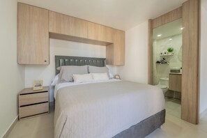A modern bedroom with a bed, a nightstand, and built-in wooden cabinets above the bed. - Very close to the beach and the historic center (Cartagena de Indias)