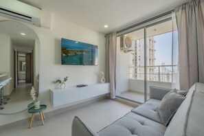A modern living room with a large window, a sofa, a small table with a plant, and a mounted TV. - Very close to the beach and the historic center (Cartagena de Indias)