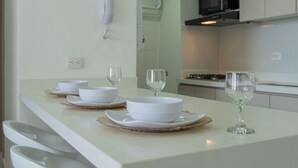 Uma cozinha moderna com armários brancos, micro-ondas e fogão. Há tigelas brancas e copos de vinho na bancada.
