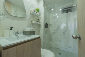 A modern bathroom with a marble sink, wooden cabinets, a glass shower enclosure, and built-in shelves with toiletries. - Very close to the beach and the historic center (Cartagena de Indias)