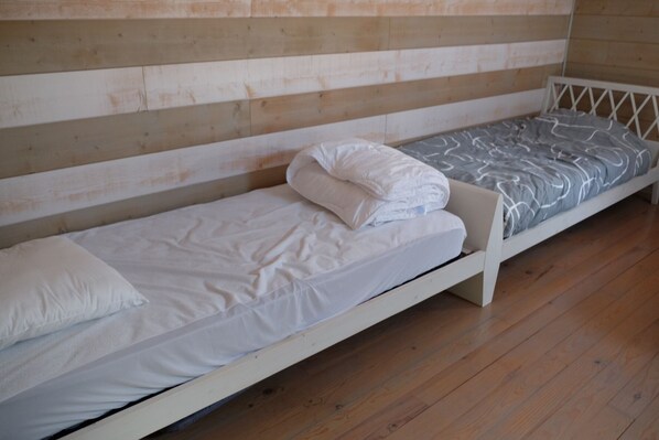 A single bed with a white mattress and pillow, a grey patterned blanket, and a wooden floor. - Duplex on the Arcachon basin (Audenge)