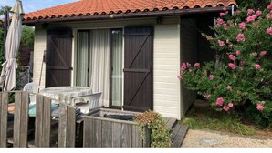 A small house with a tiled roof, a wooden fence, and a garden with pink flowers.