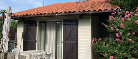 A small house with a tiled roof, a wooden fence, and a garden with pink flowers.
