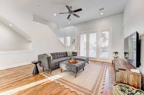 A spacious living room with a sectional sofa, a wooden coffee table, and a TV on a wooden stand. - Modern Midtown Getaway with City Views (Houston)