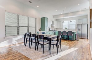 A modern kitchen with white cabinets, a central island, and a dining area with a table and chairs. - Modern Midtown Getaway with City Views (Houston)