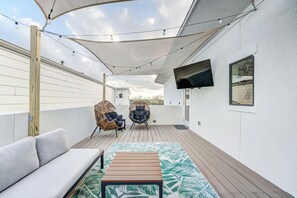 A covered outdoor deck with a sofa, two chairs, a table, and a TV mounted on the wall. - Modern Midtown Getaway with City Views (Houston)