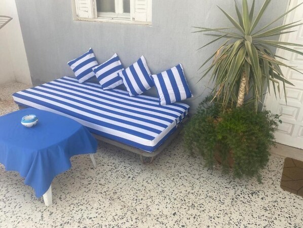 A bed with blue and white striped bedding, a small table with a blue tablecloth, and a potted plant beside the bed. - Dar koukaa (Tataouine)