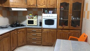 A kitchen with wooden cabinets, a microwave, an oven, and a table with a chair.