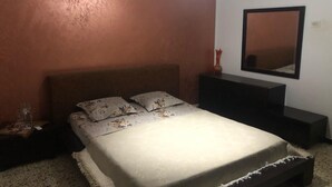 A bedroom with a bed, nightstand, dresser, and a mirror on the wall.
