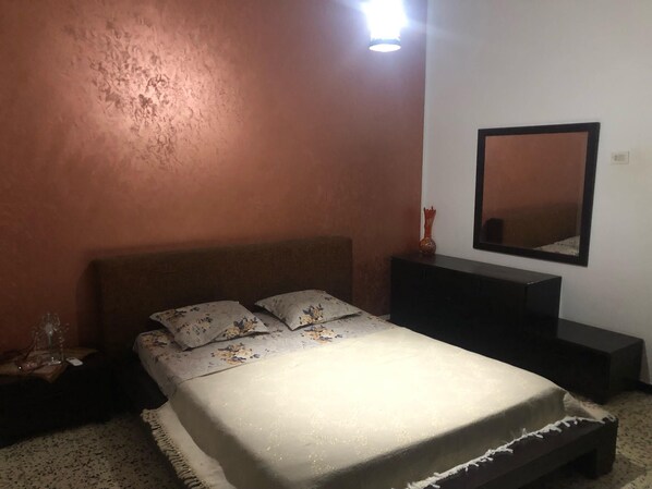 A bedroom with a bed, nightstand, dresser, and a mirror on the wall.