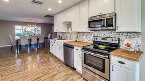 Una cucina moderna con mobili bianchi, elettrodomestici in acciaio inossidabile e un piano di lavoro in legno.