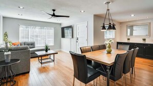 Ein modernes Wohnzimmer mit grauem Sofa, Couchtisch und Essbereich mit Holztisch und schwarzen Stühlen.