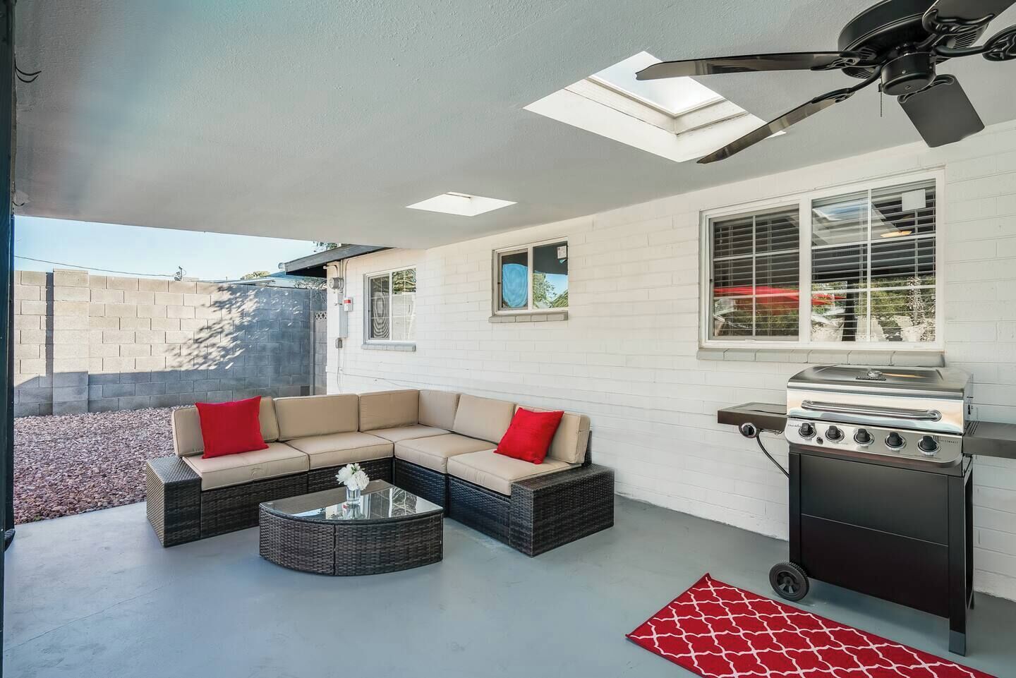 A covered patio with a sectional sofa, a round coffee table, a grill, and a ceiling fan.