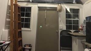 Een kamer met een schuine kap, een hoogslaper, een ladder, een deur, een klein tafeltje en een prullenbak.