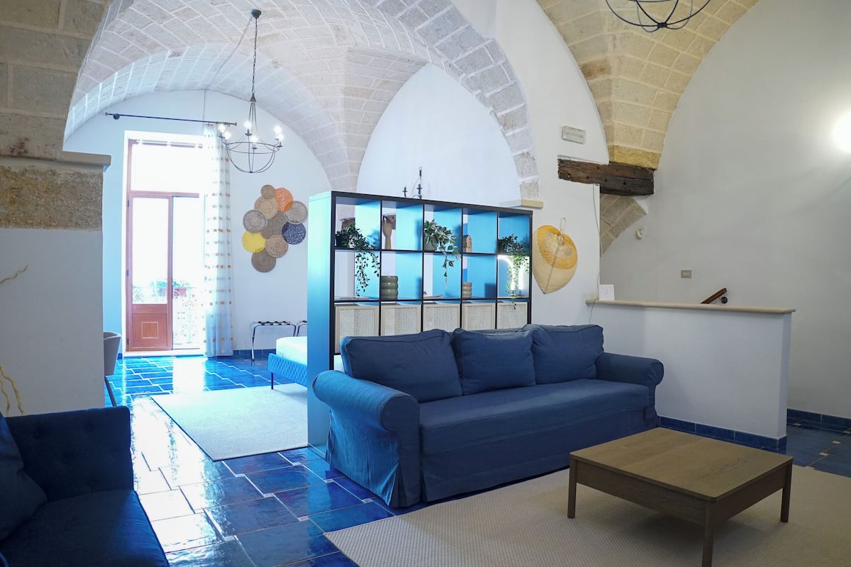 A spacious living room with a blue sofa, a wooden coffee table, and a decorative wall unit with plants.
