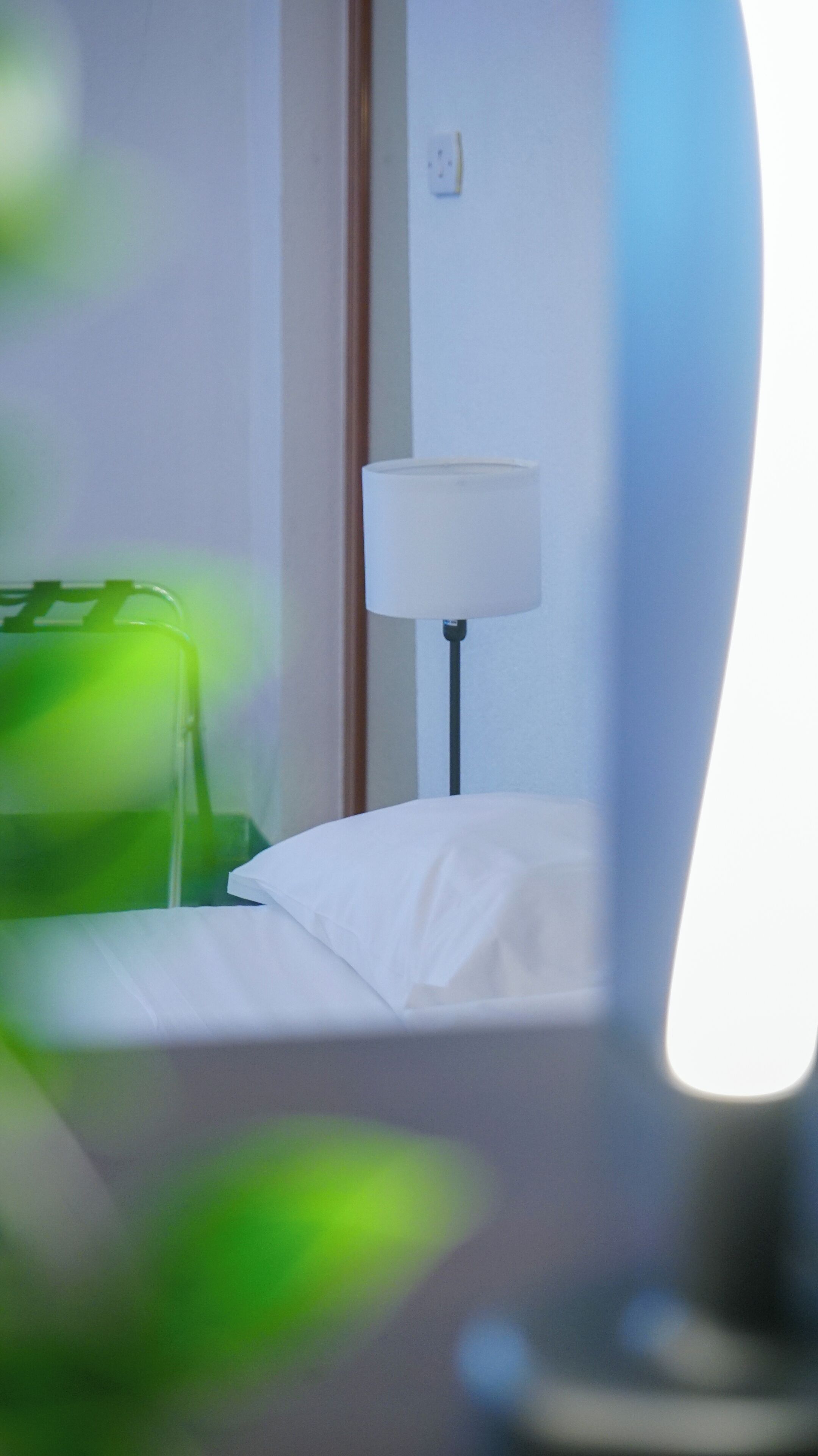 A hotel room with a bed, a lamp, and a green bag.