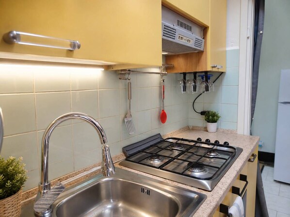 A kitchen with a stainless steel sink, a gas stove, and a hanging utensil rack.