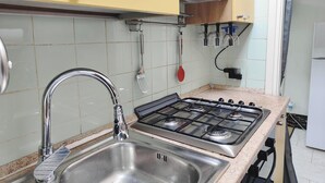 A kitchen with a stainless steel sink, a gas stove, and a variety of utensils hanging on the wall.