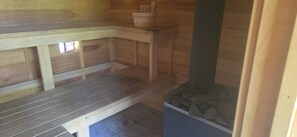 Puisesta laudelankusta rakennettu sauna, kivinen allas ja puinen seinä.