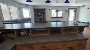 A kitchen with a pool table, wooden cabinets, and blue pendant lights.