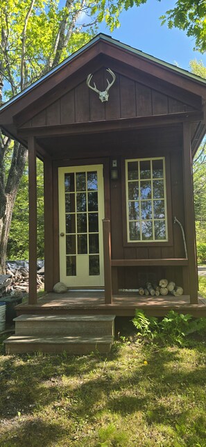 Eine kleine Holzhütte mit einer Haustür, einem Fenster und einer Veranda mit Baumstämmen.