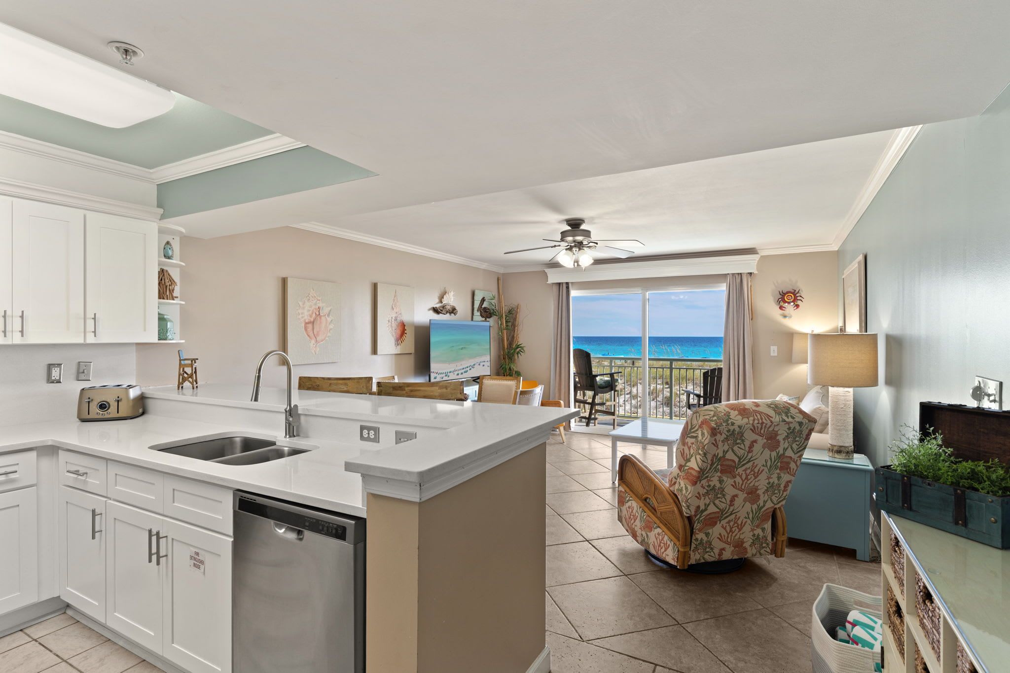 A modern kitchen with a central island, a dining area with a view of the ocean, and a living space with a ceiling fan.