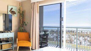 Un balcone con vista sulla spiaggia e sullo skyline cittadino, un divano, un tavolo e una TV su un mobile.