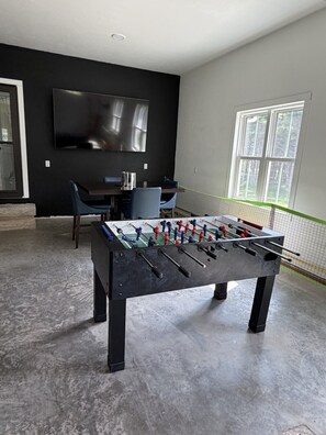 Une chambre moderne équipée d’un baby-foot, d’un téléviseur à écran plat et d’une fenêtre offrant une vue agréable.