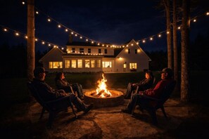 Une maison avec un foyer au centre, entouré de chaises, et des guirlandes lumineuses suspendues au-dessus.
