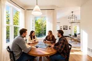 Un groupe de personnes est assis autour d’une table ronde dans une pièce bien éclairée, dotée de grandes fenêtres, d’un luminaire suspendu et d’une cheminée bien visible.