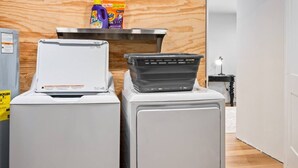 A laundry area with two washing machines, a dryer, and a shelf with detergent bottles. - Luxury Cottage Escape | 2 King Beds + Fire Pit (Sister Bay)
