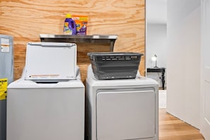 Un espace buanderie comprenant deux machines à laver, un sèche-linge et une étagère avec des bouteilles de lessive.