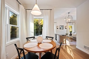 Un coin repas avec une table ronde, des chaises, un luminaire suspendu et, en arrière-plan, une vue sur un salon.