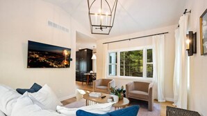 A modern living room with a sofa, armchair, coffee table, and a painting of a cityscape. - Luxury Cottage Escape | 2 King Beds + Fire Pit (Sister Bay)