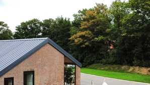 Een gebouw van baksteen met een schuin dak, een klein terras en een grindpad met buitenmeubilair.