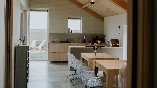 Een ruime keuken in loft-stijl, met hoge plafonds, grote ramen en een eethoek met moderne stoelen.