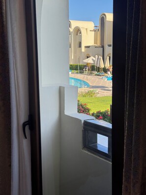 A view from a window with a door, overlooking a pool area with umbrellas and a building with arches. - Sahl Hasheesh Finest Chalet Gravity 5 star beachfront hotel - NON EGYPTIAN ONLY (Hurghada)