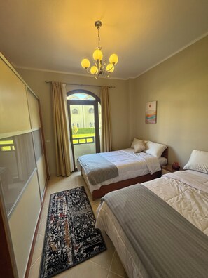 A hotel room with two beds, a chandelier, a view of a building through a door, and a painting on the wall. - Sahl Hasheesh Finest Chalet Gravity 5 star beachfront hotel - NON EGYPTIAN ONLY (Hurghada)